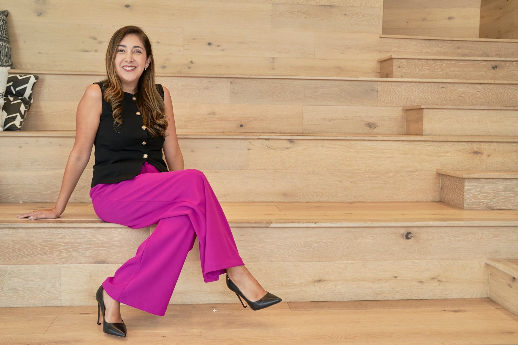 Adriana Flores smiling, seated on light wooden steps