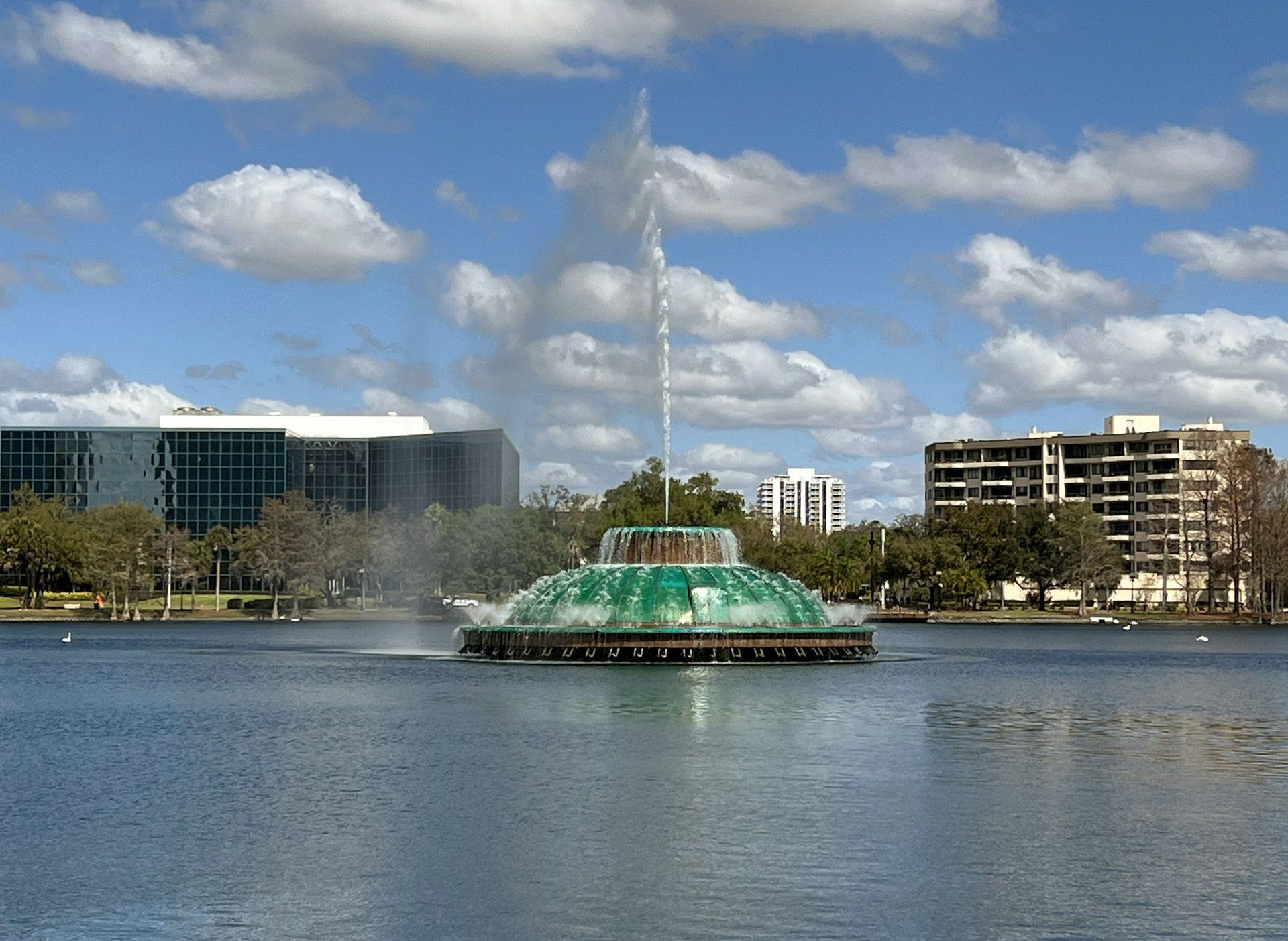 The Lake Eola fountain in downtown Orlando on a sunny day, with the lake in front and buildings behind