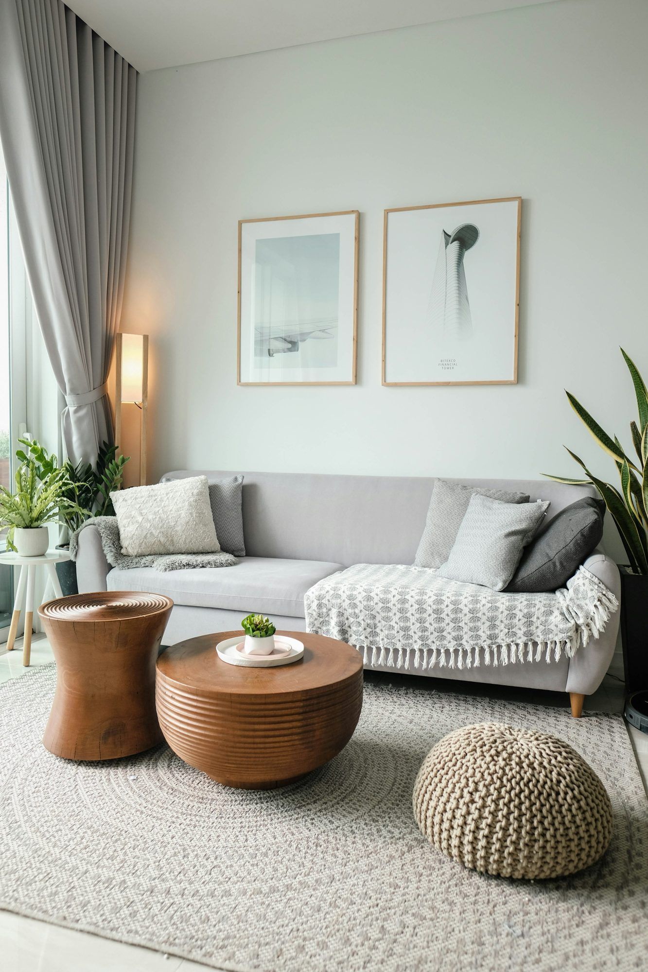 A bright, staged living room with a gray sofa, round wooden tables and framed prints