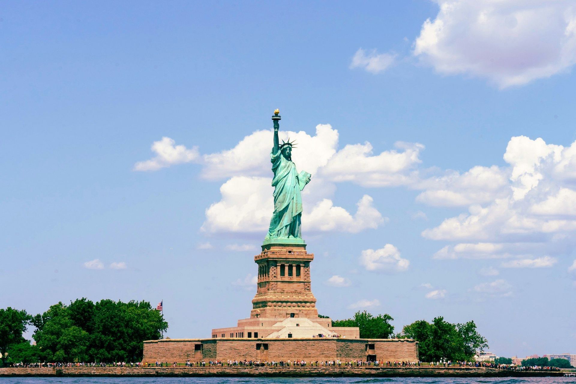 The Statue of Liberty on Liberty Island in New York Harbor, under a blue sky with white clouds