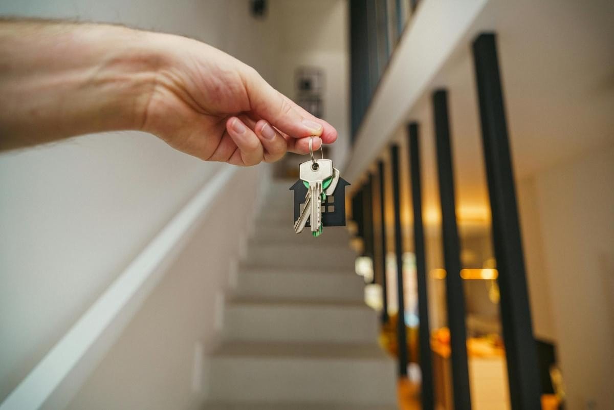 A hand holding a set of house keys on a house-shaped key ring